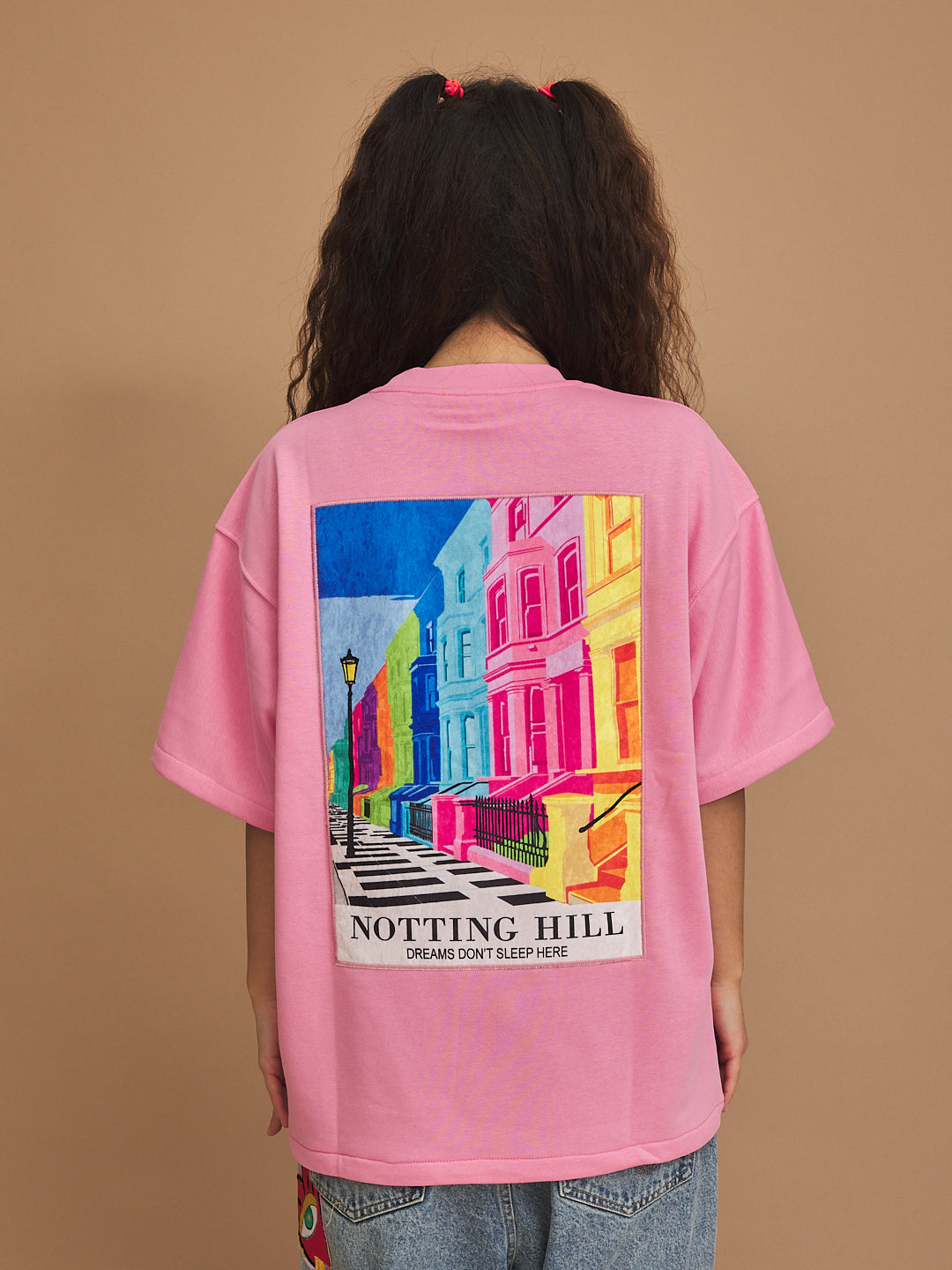 Person wearing a pink t-shirt with a colorful 'Notting Hill' design on the back against a brown background