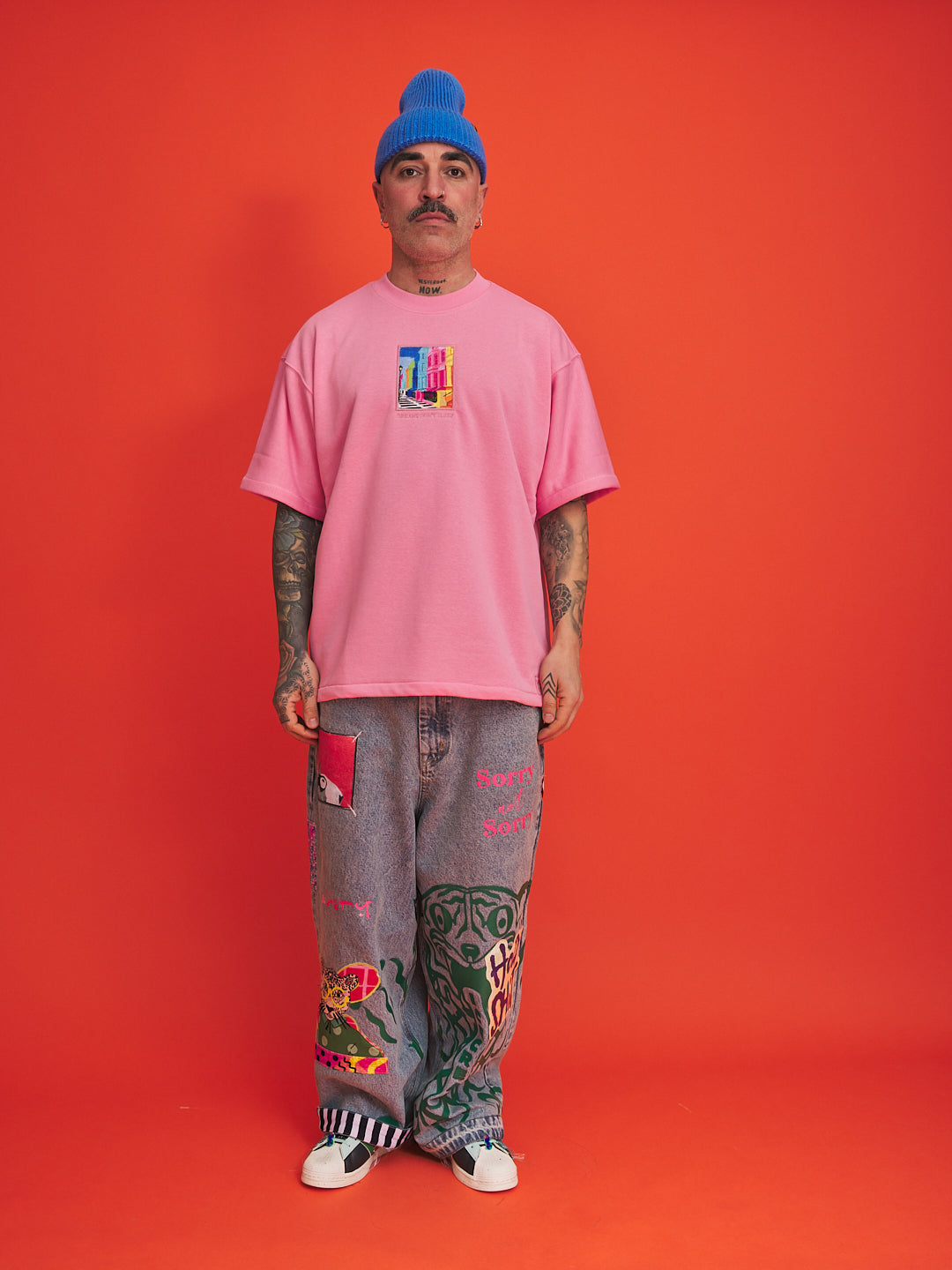 Person wearing a pink t-shirt and gray pants with colorful designs on an orange background