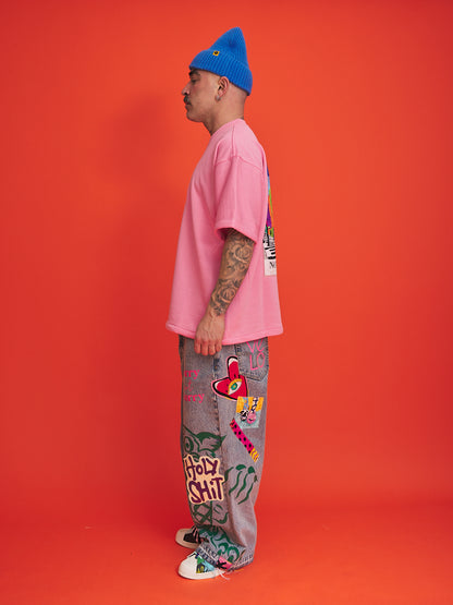 Person wearing a pink shirt, blue beanie, and gray pants with colorful designs on an orange background