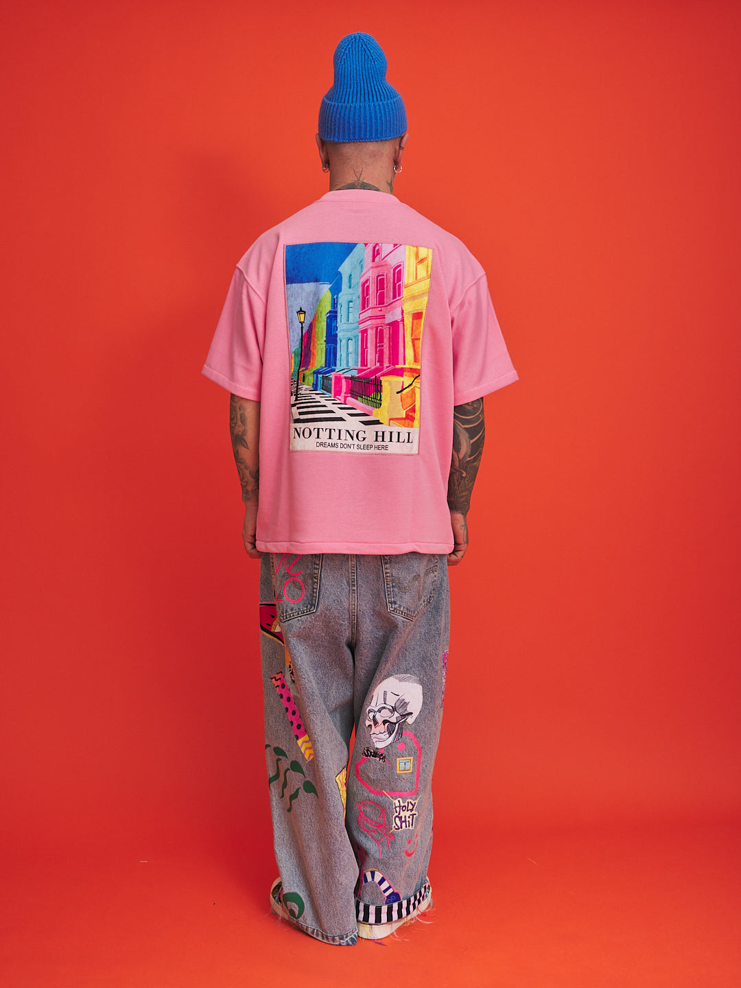 Person wearing a pink t-shirt with colorful graphic design and blue beanie on an orange background