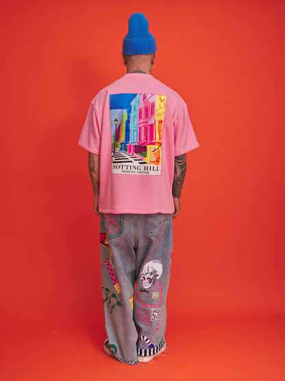 Person wearing a pink t-shirt with colorful graphic design and blue beanie on an orange background