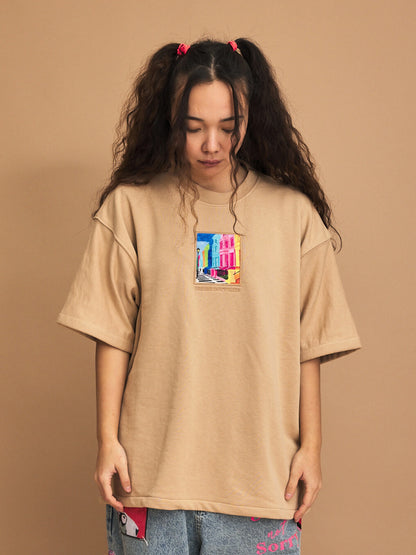 Person wearing a cream t-shirt with a colorful graphic on a brown background