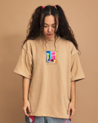 Person wearing a cream t-shirt with a colorful graphic on a brown background