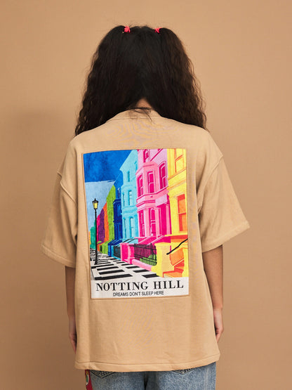 Person wearing a beige t-shirt with a colorful 'Notting Hill' graphic on the back against a brown background