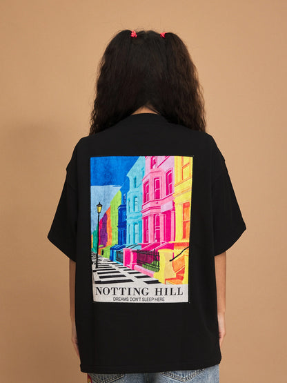 Person wearing a black t-shirt with a colorful 'Notting Hill' design on the back against a brown background