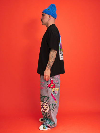 Person wearing a black t-shirt, colorful pants, and a blue beanie against an orange background