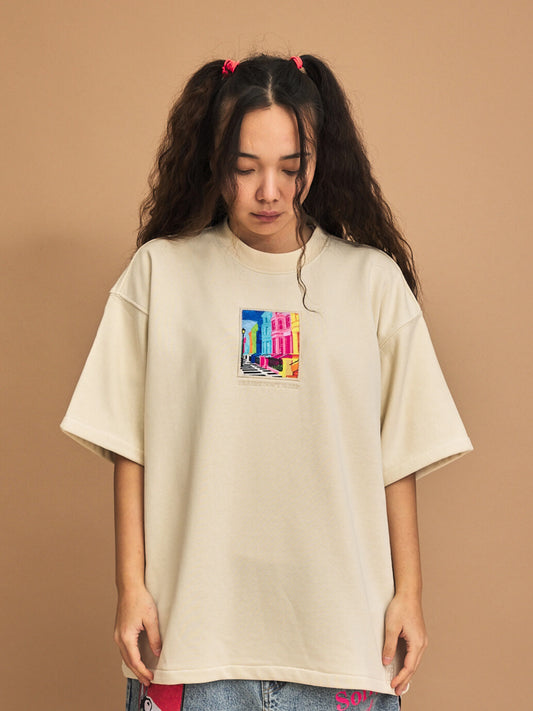 Person wearing a cream t-shirt with a colorful graphic on a brown background