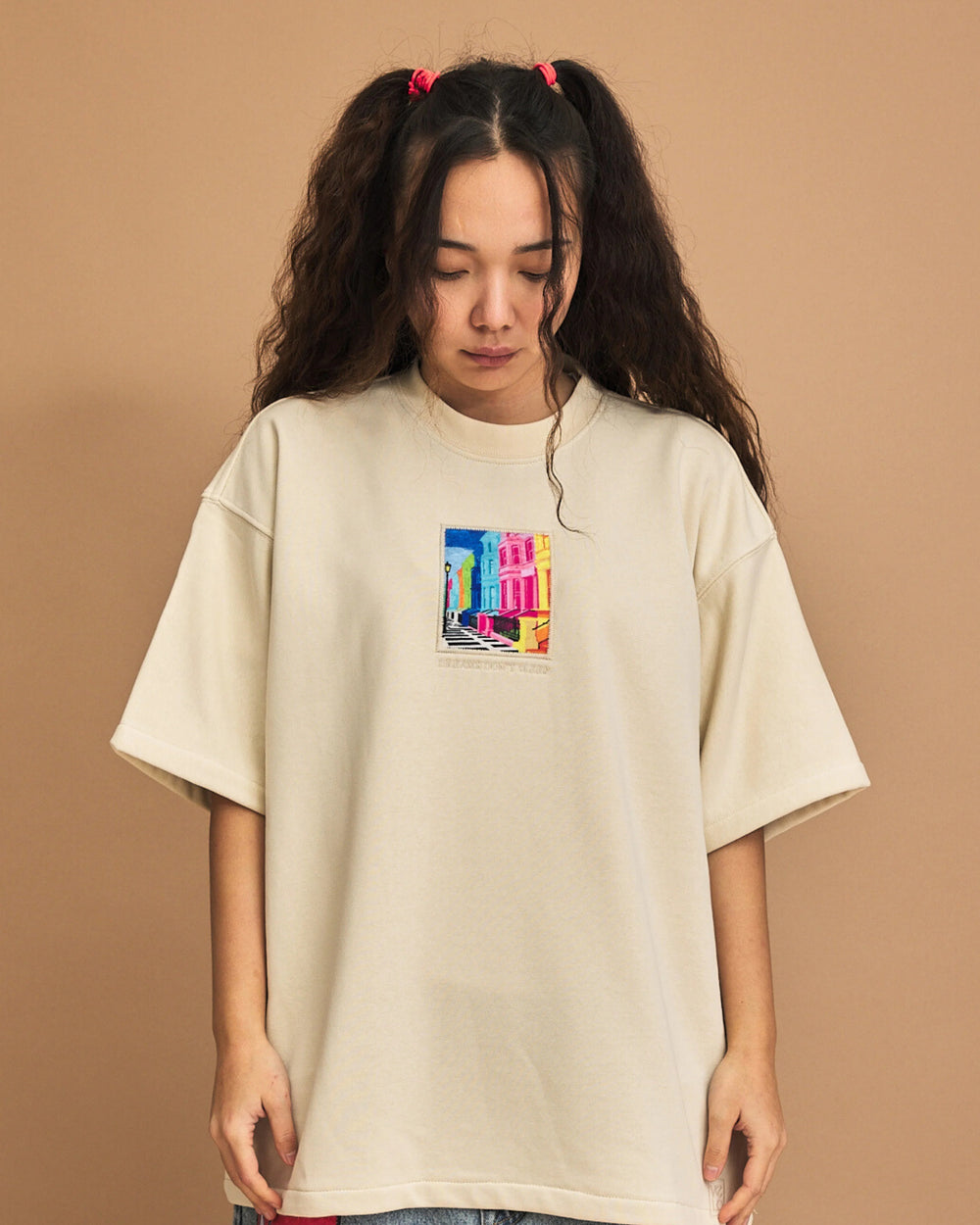 Person wearing a cream t-shirt with a colorful graphic on a brown background