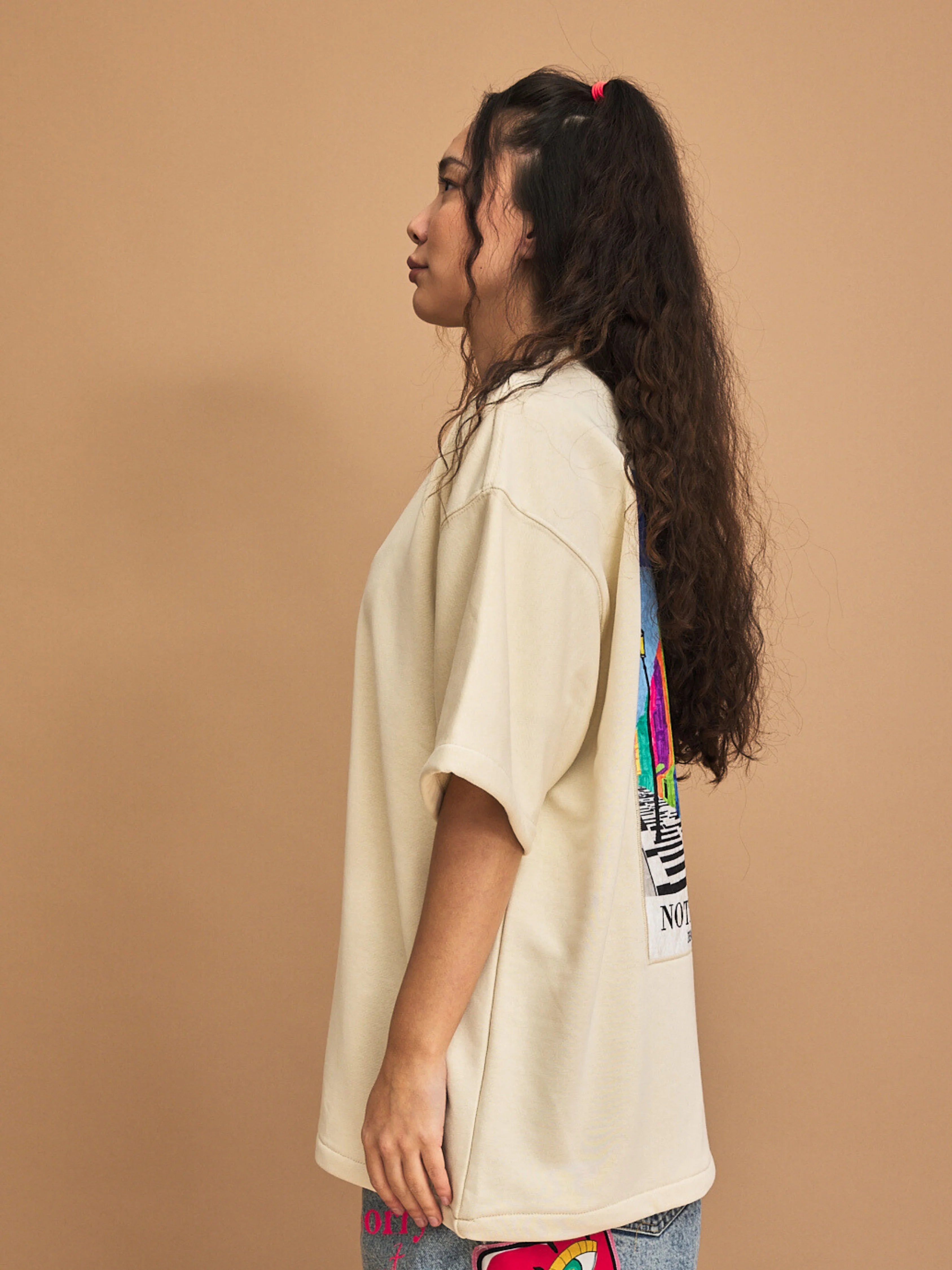 Woman wearing a cream t-shirt with colorful graphics on a brown background