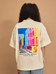 Person wearing a cream t-shirt with a colorful 'Notting Hill' design on the back against a brown background