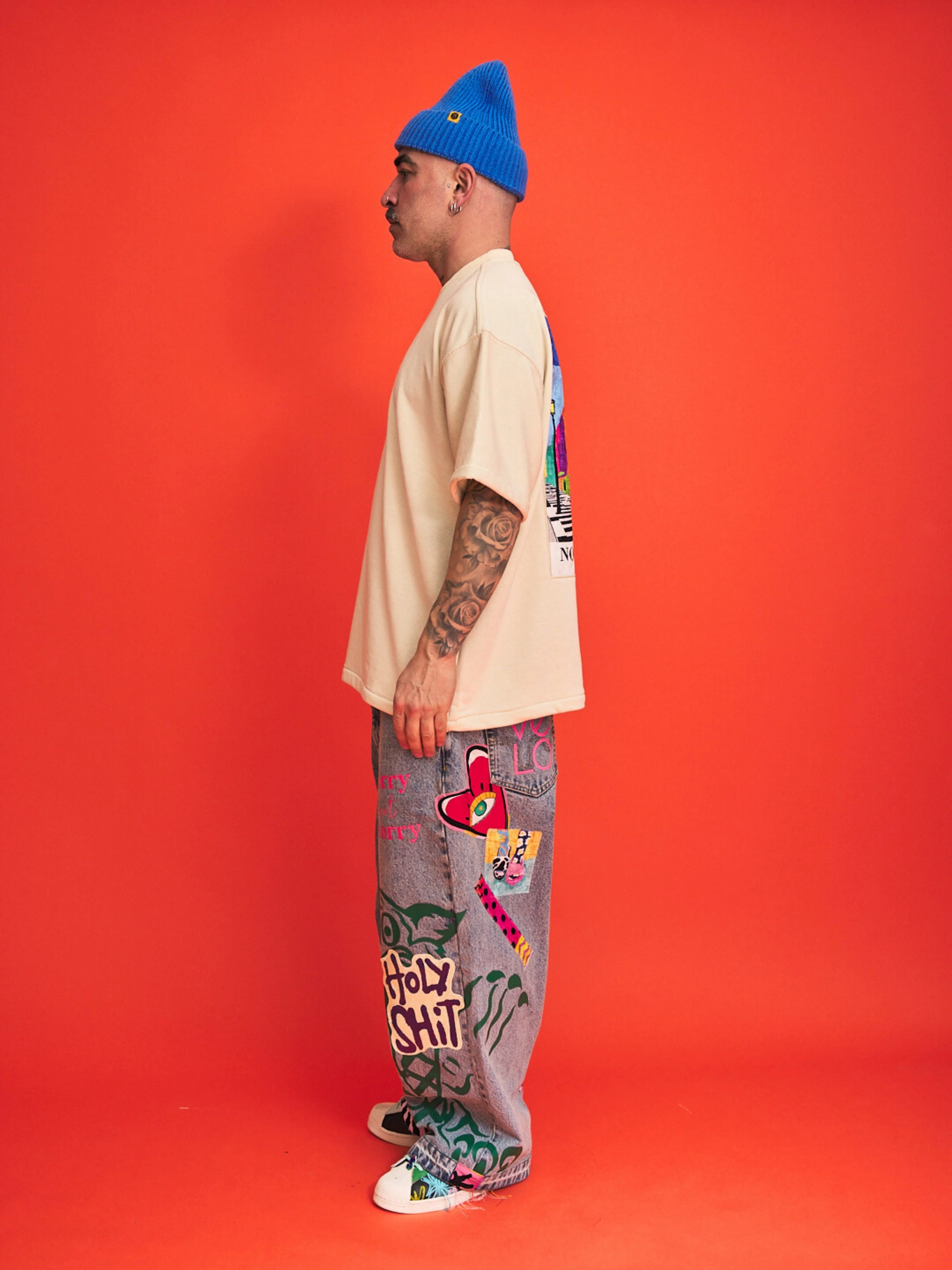 Person wearing a blue beanie, cream t-shirt, and colorful pants with text on an orange background