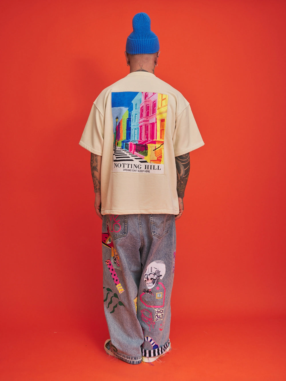 Person wearing a cream t-shirt with a colorful graphic and text, standing against an orange background
