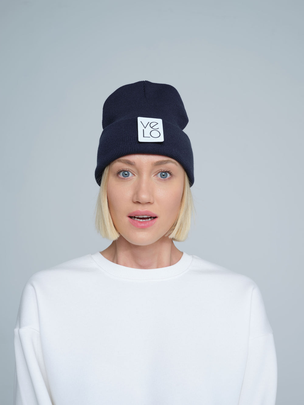 Person wearing a navy beanie with a logo on a gray background