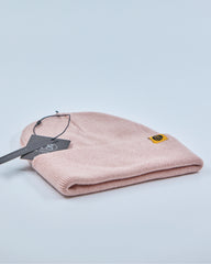 Dusty rose pink beanie with a tag on a light gray background