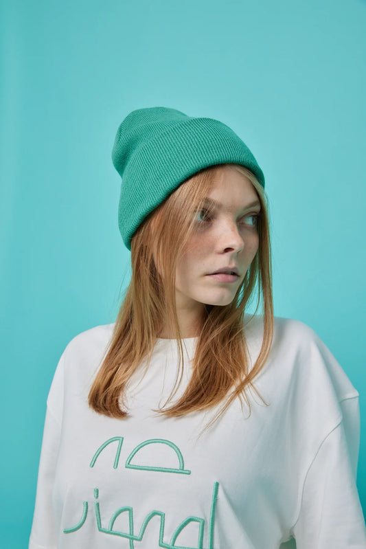 Person wearing a white sweatshirt with green text and a green beanie against a teal background