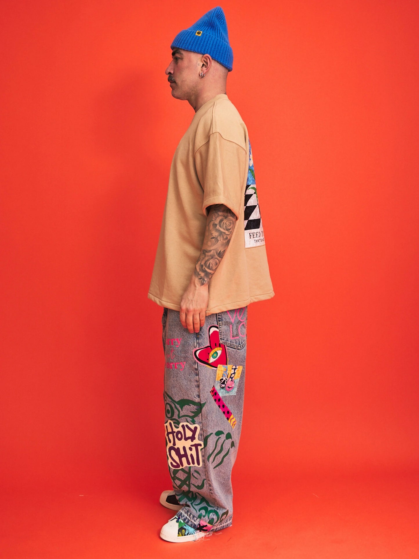 Person wearing a beige shirt, blue beanie, and colorful pants with text on an orange background