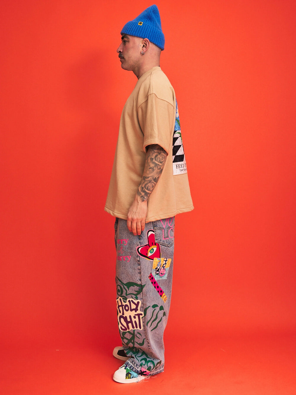 Person wearing a beige shirt, blue beanie, and colorful pants with text on an orange background