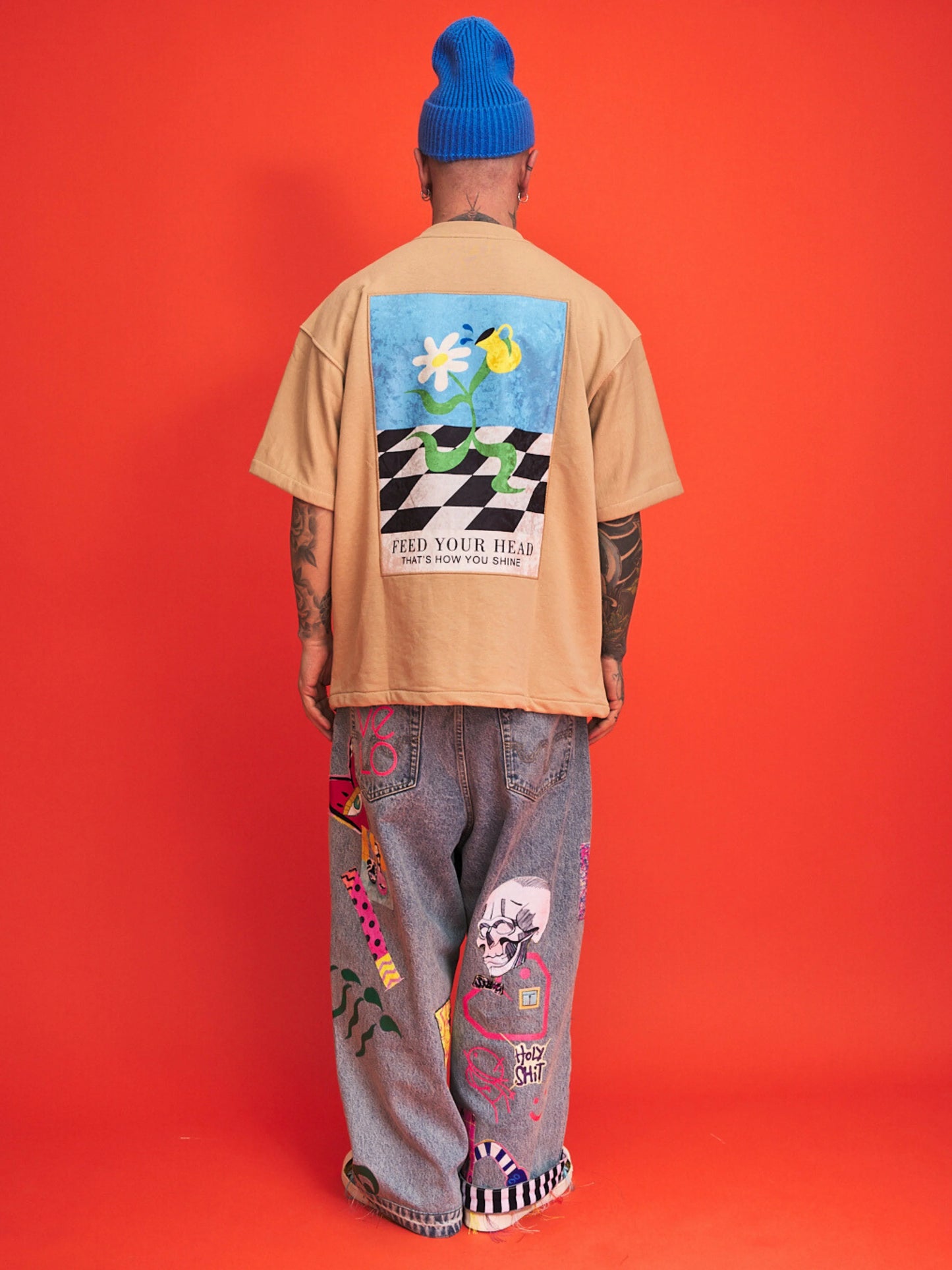 Person wearing a beige t-shirt with a colorful graphic on the back against an orange background