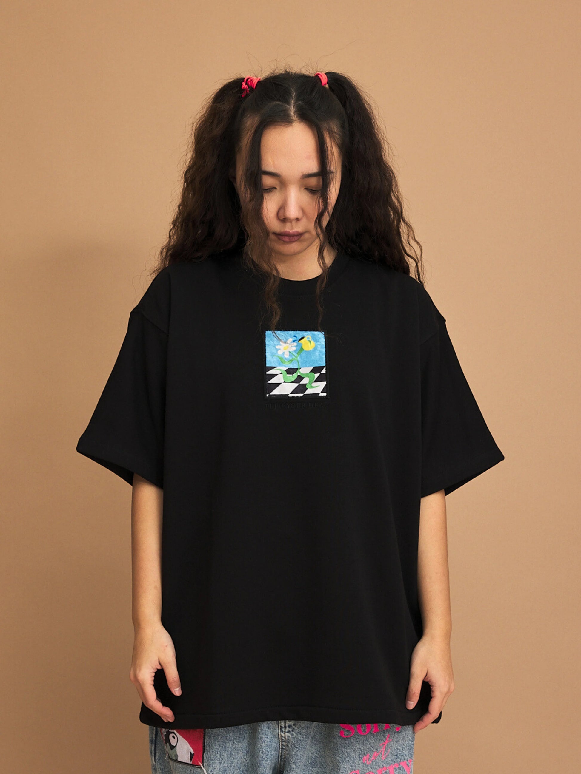 Person wearing a black t-shirt with a small graphic on a brown background