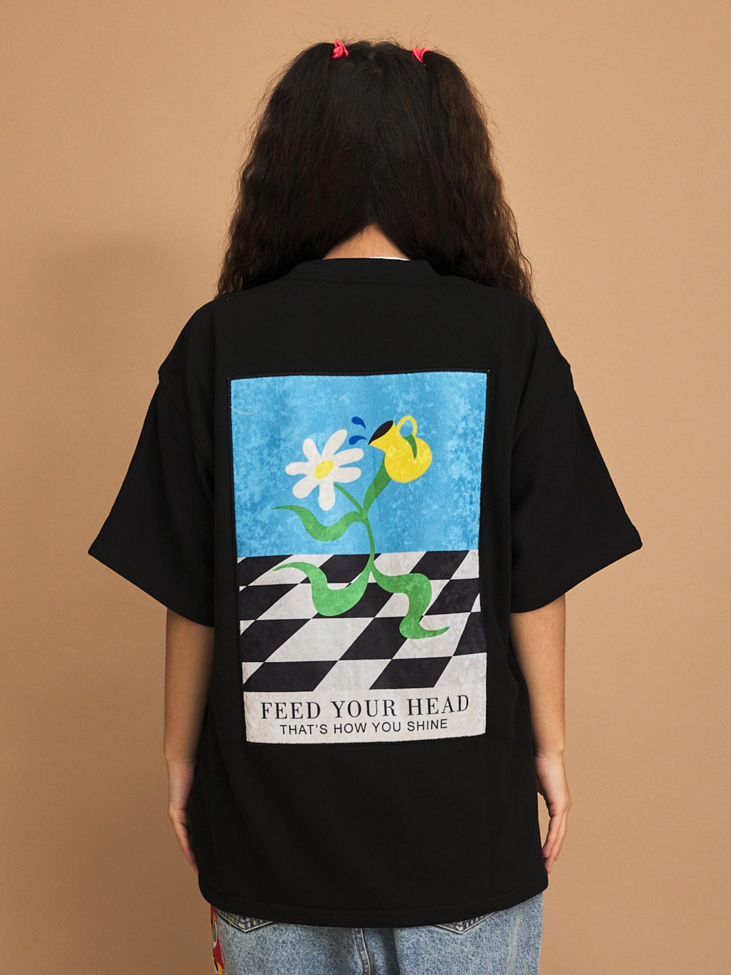 Person wearing a black t-shirt with a colorful graphic and text on the back against a brown background