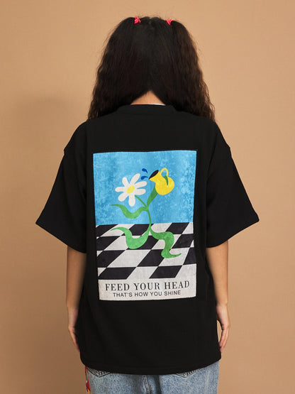 Person wearing a black t-shirt with a colorful graphic and text on the back against a brown background