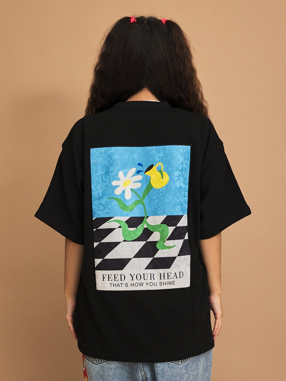 Person wearing a black t-shirt with a colorful graphic and text on the back against a brown background