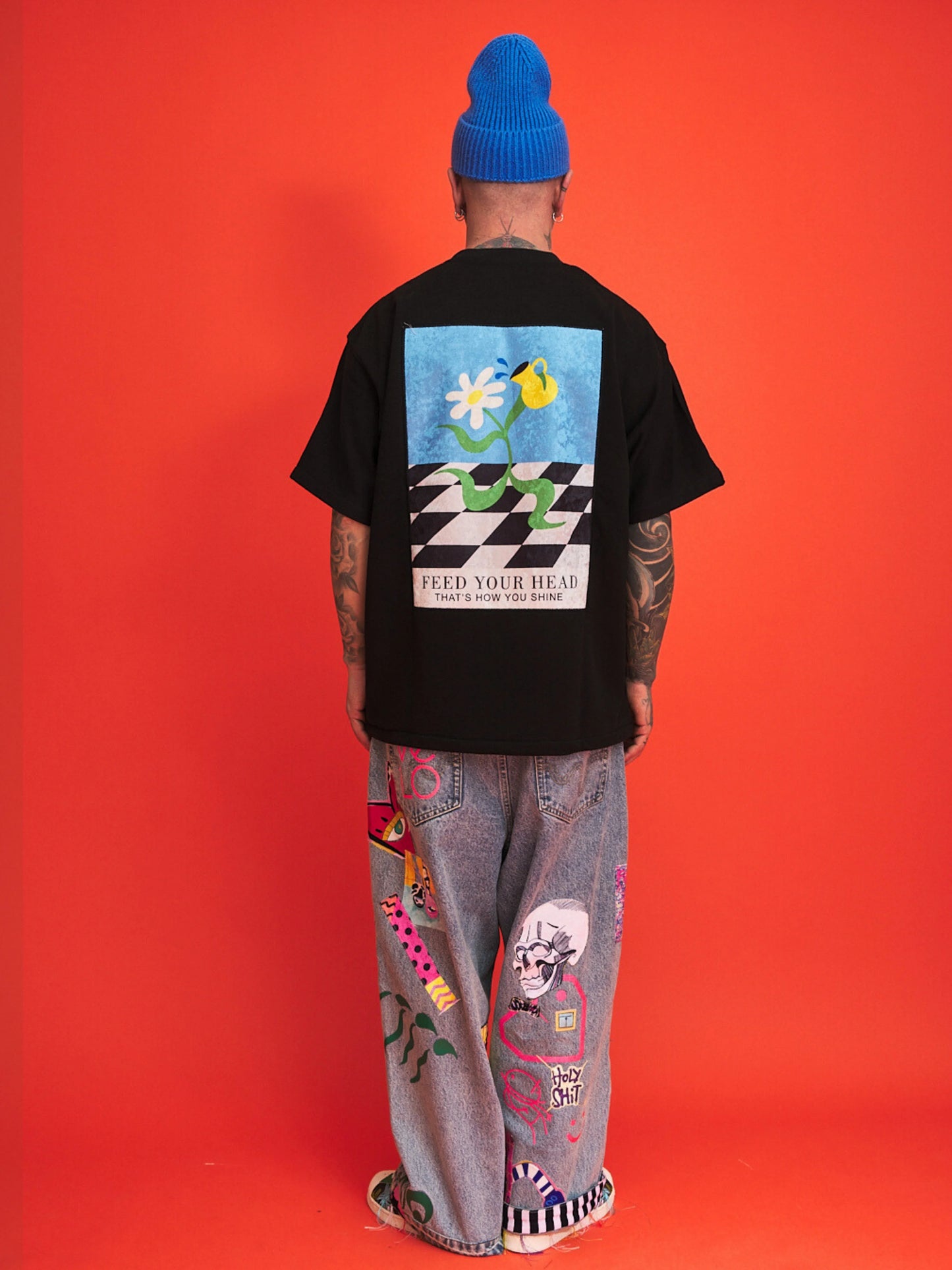 Person wearing a black t-shirt with a colorful graphic design on the back, standing against an orange background.