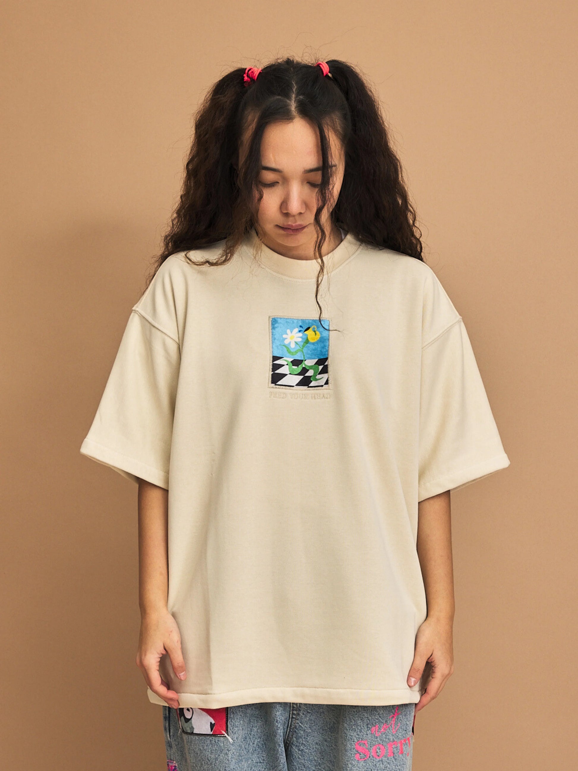 Person wearing a beige oversized t-shirt with a graphic design on a brown background