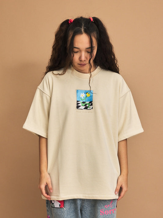 Person wearing a beige oversized t-shirt with a graphic design on a brown background