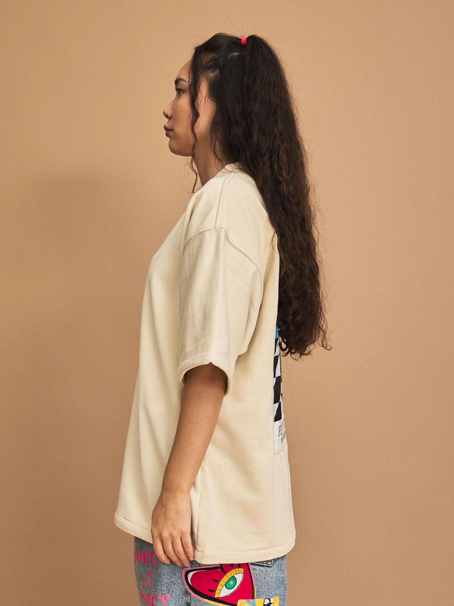 Woman wearing a cream oversized t-shirt against a brown background