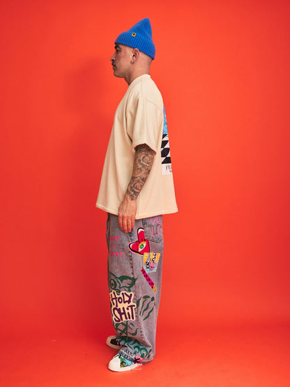 Person wearing a blue beanie, cream shirt, and colorful pants against an orange background