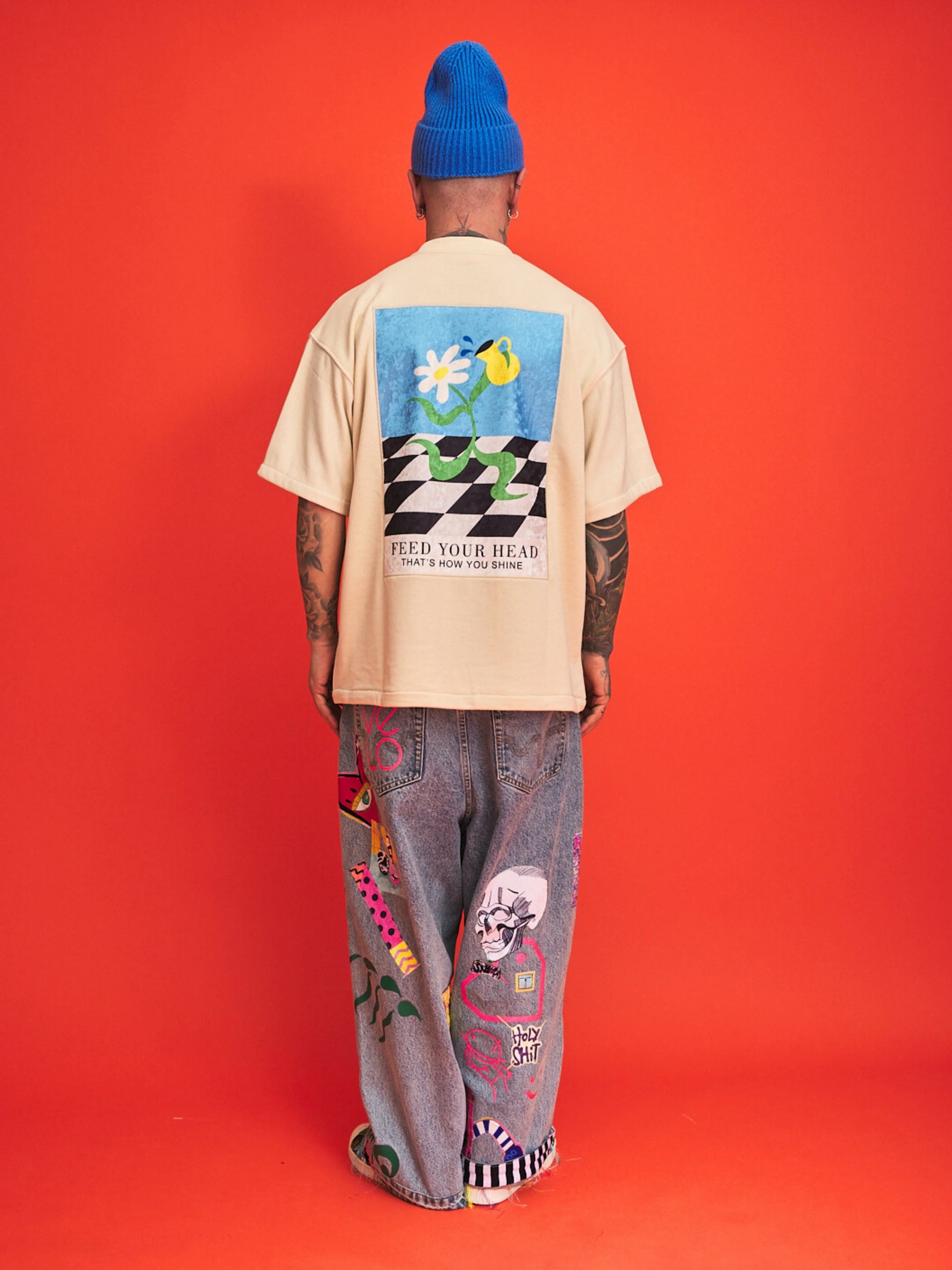 Person wearing a cream t-shirt with a colorful graphic and text, standing against an orange background