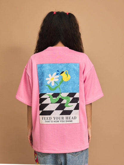 Person wearing a pink t-shirt with a graphic design on the back against a brown background