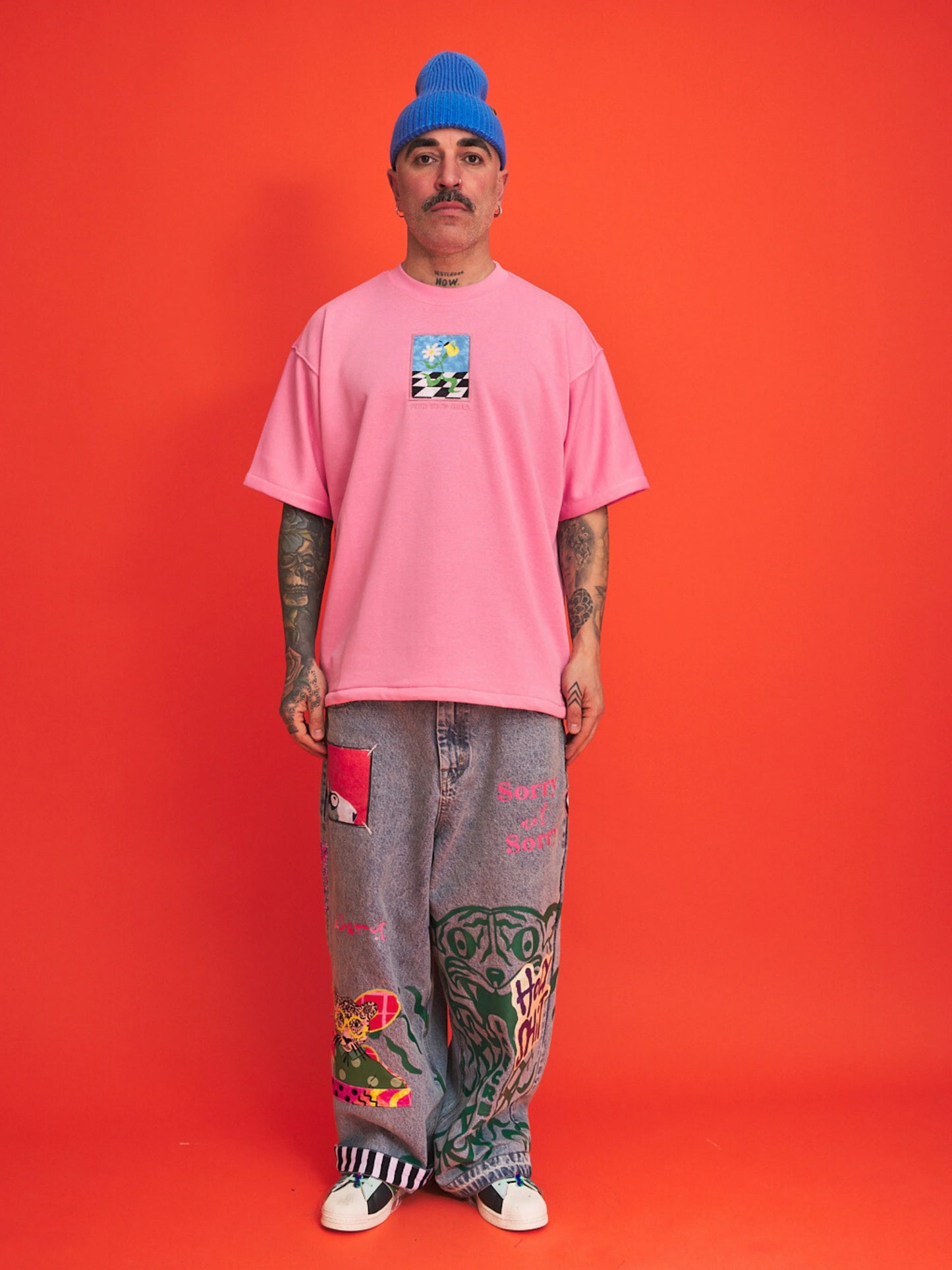 Person wearing a pink t-shirt and colorful pants against an orange background