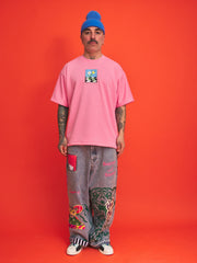 Person wearing a pink t-shirt and colorful pants against an orange background