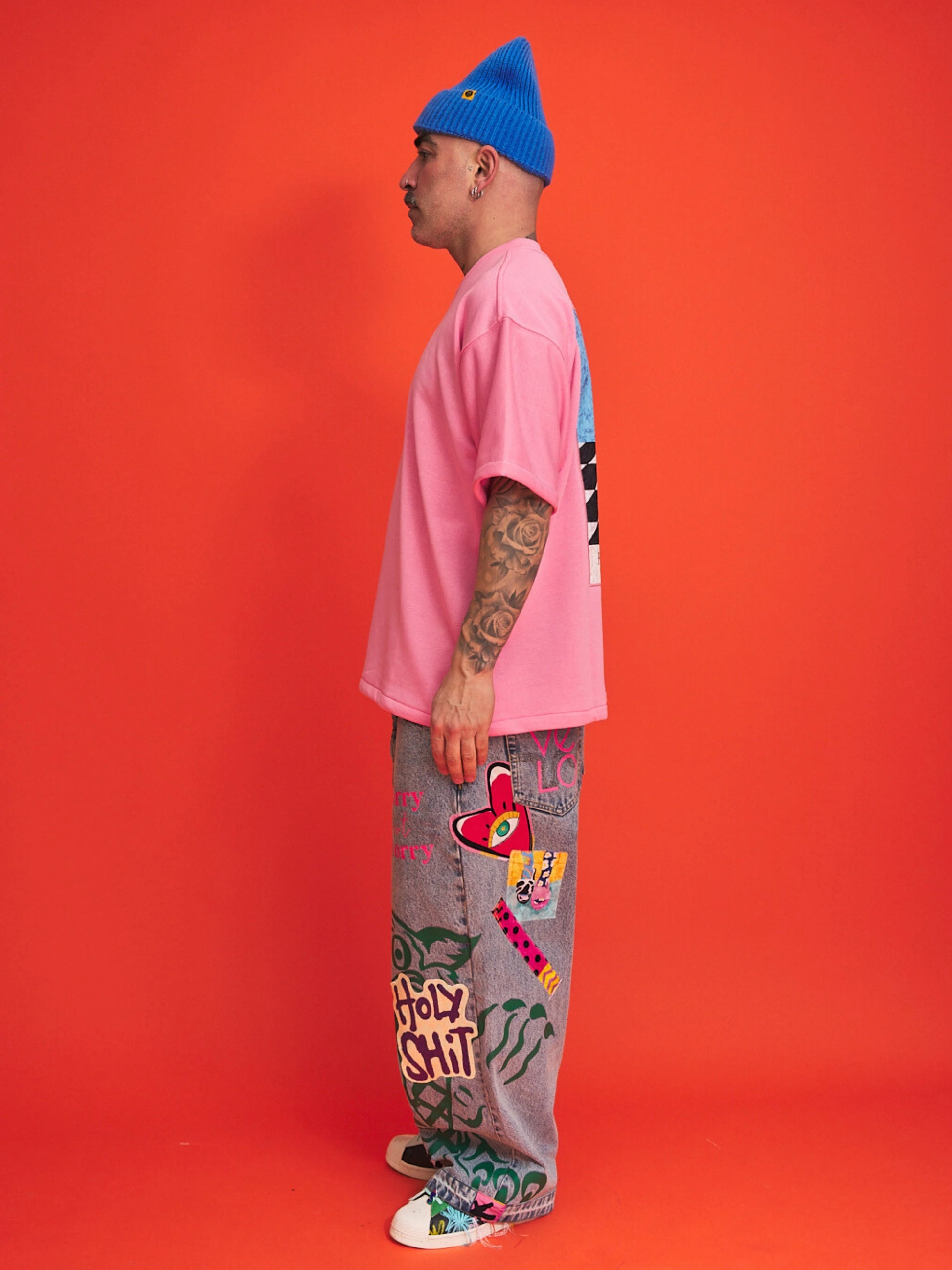 Person wearing a pink shirt, blue beanie, and colorful pants with text on an orange background