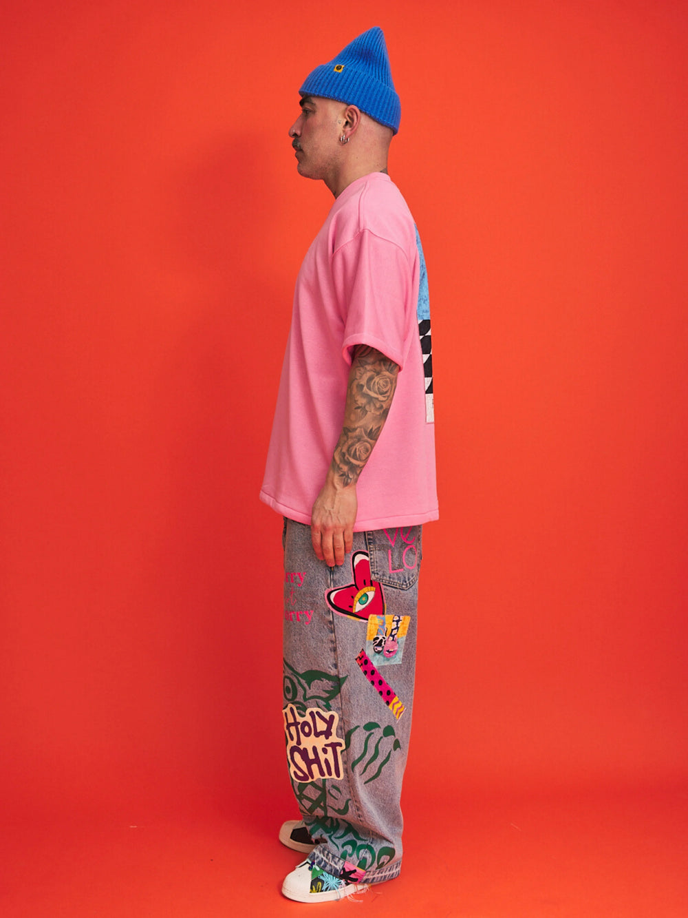 Person wearing a pink shirt, blue beanie, and colorful pants with text on an orange background