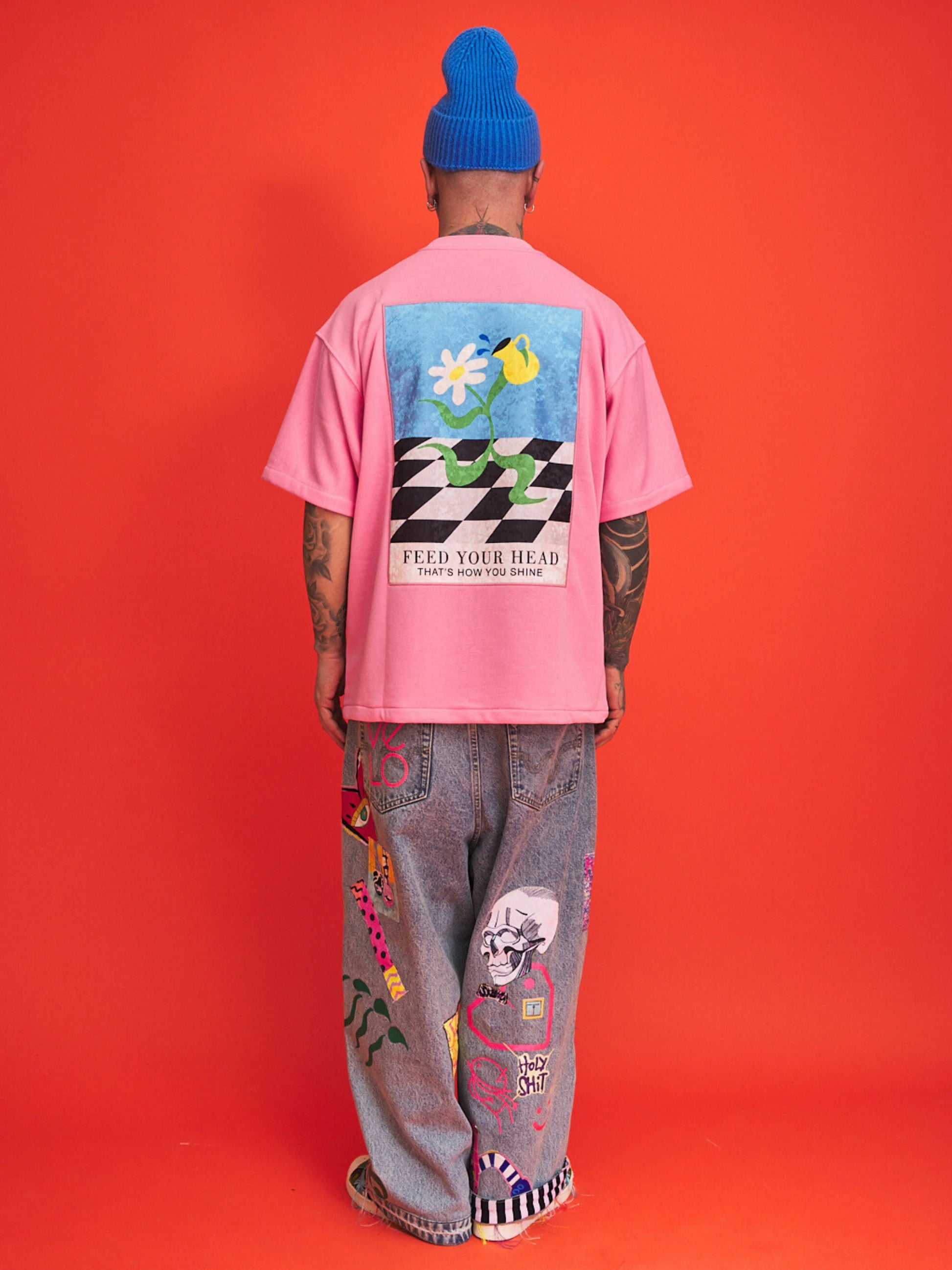 Person wearing a pink t-shirt with a colorful graphic and text, standing against an orange background.