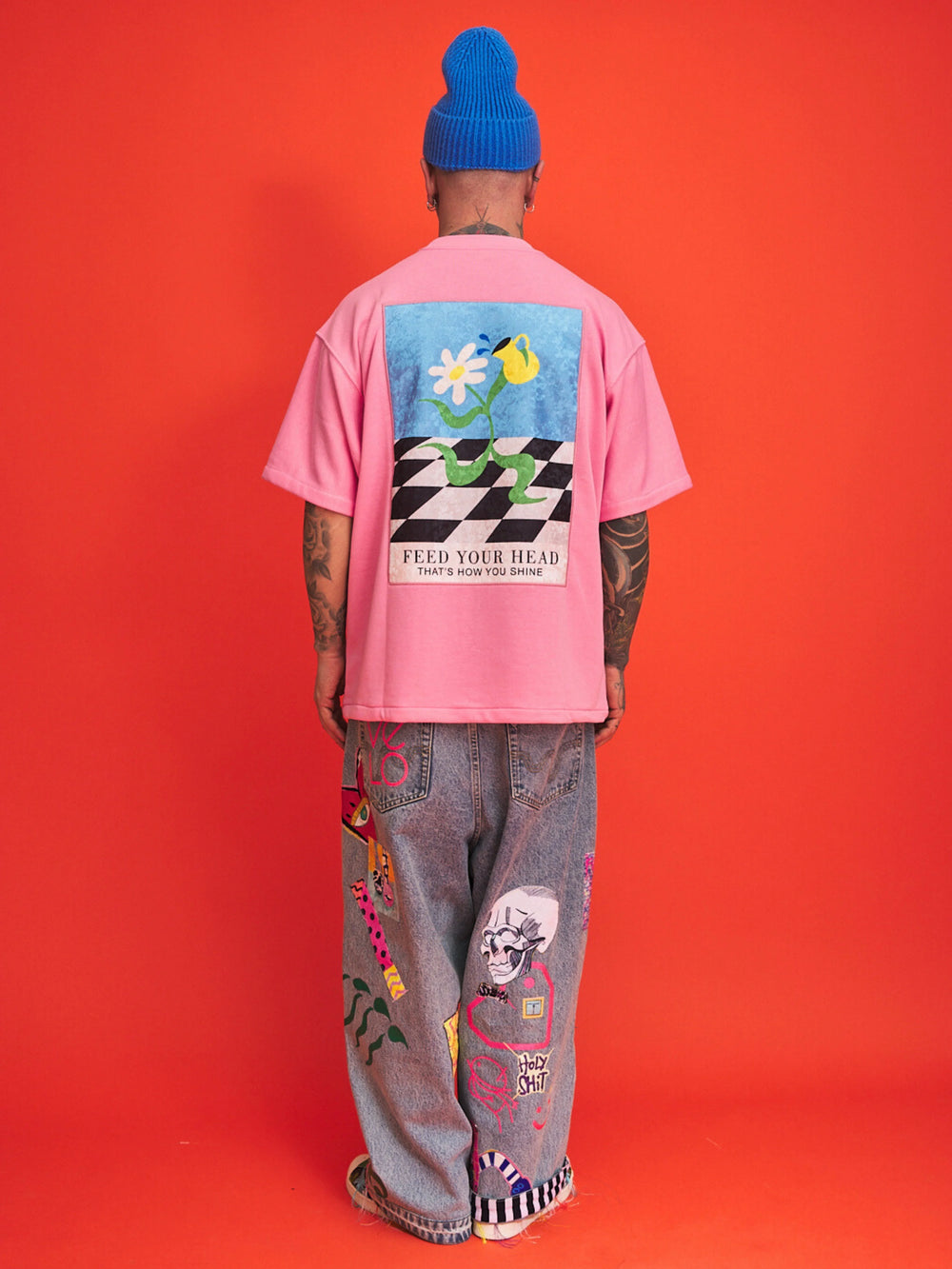 Person wearing a pink t-shirt with a colorful graphic and text, standing against an orange background.