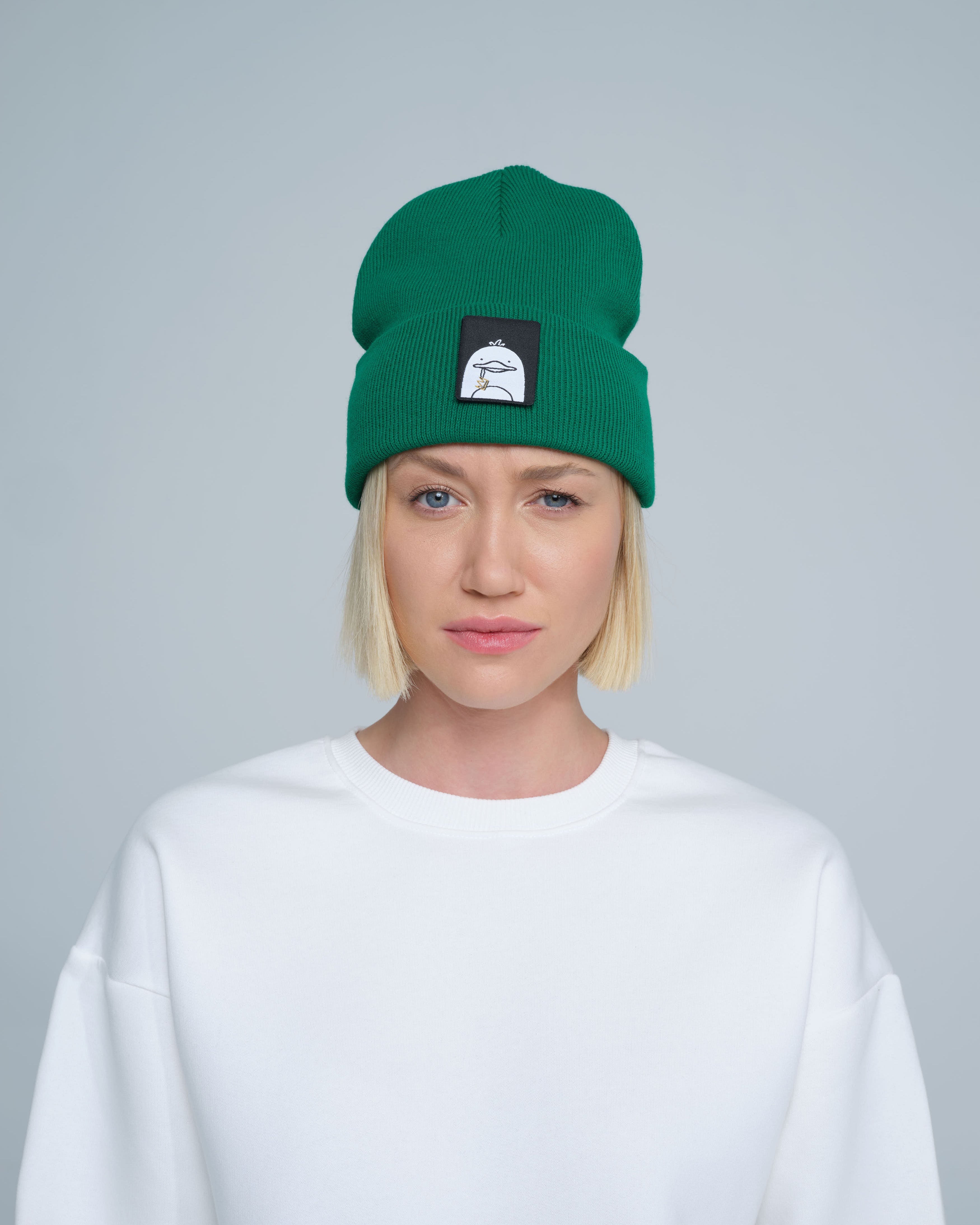 A person wearing green beanie with a duck patch on a gray background