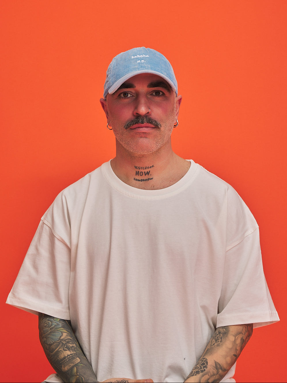 Man wearing a baby blue cap 'hahaha no' text on it and white t-shirt against an orange background