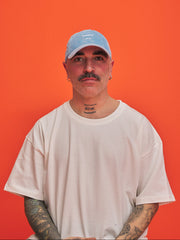 Man wearing a baby blue cap 'hahaha no' text on it and white t-shirt against an orange background