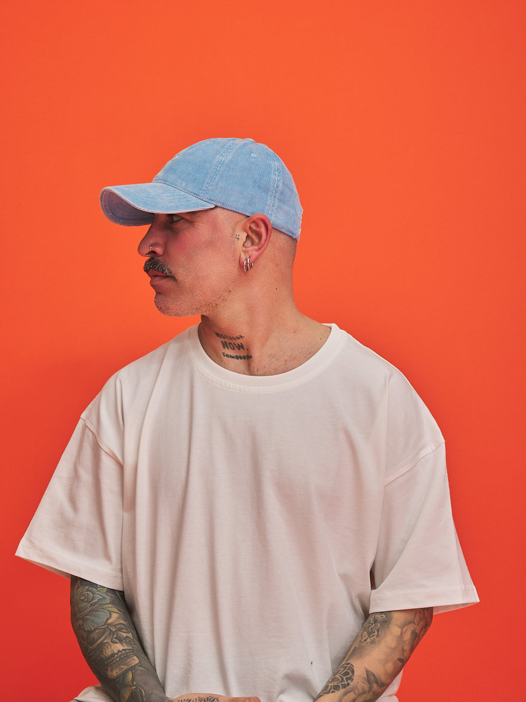 Male model wearing a baby blue cap and white t-shirt against an orange background