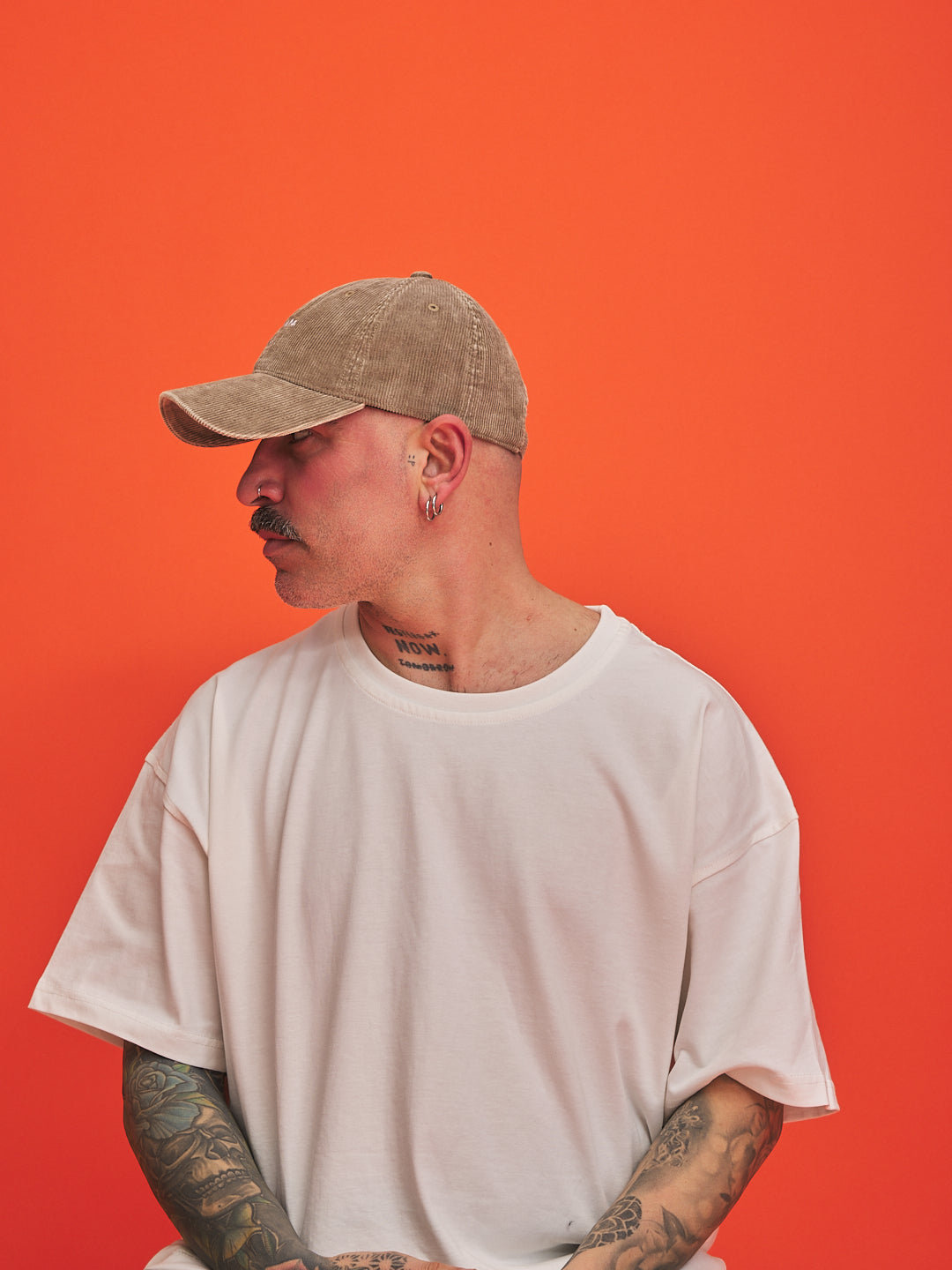 Person wearing a beige cap and white t-shirt against an orange background