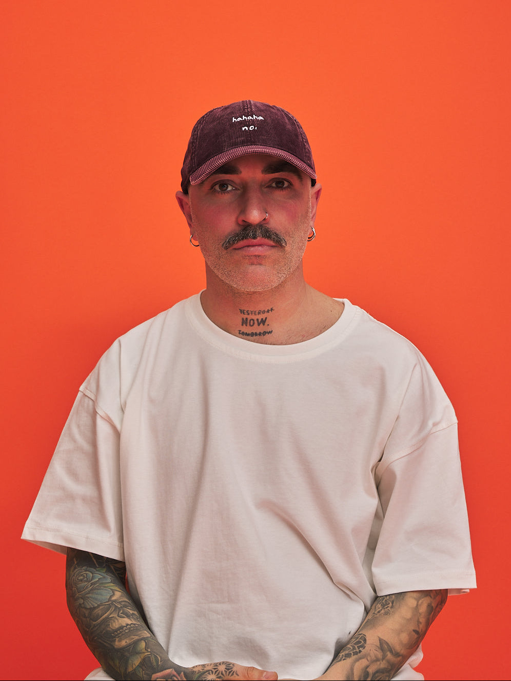 Man wearing a white t-shirt and Hahaha No Burgundy Corduroy Cap against an orange background