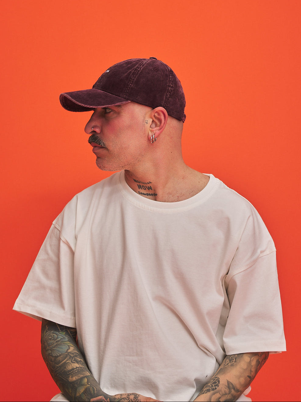 Person wearing a white t-shirt and Hahaha No Burgundy Corduroy Cap against an orange background
