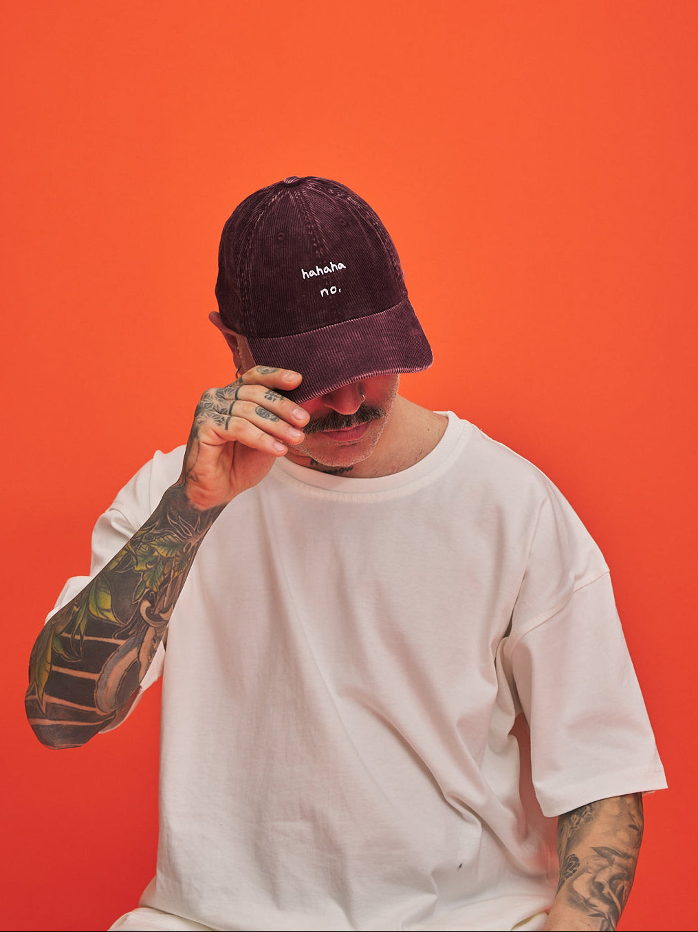 Person wearing Hahaha No Burgundy Corduroy Cap and white t-shirt against an orange background