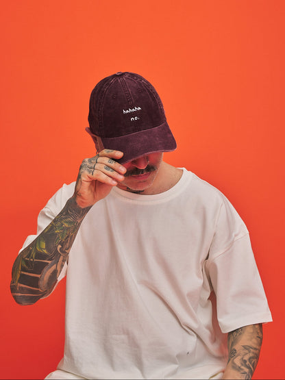 Person wearing Hahaha No Burgundy Corduroy Cap and white t-shirt against an orange background