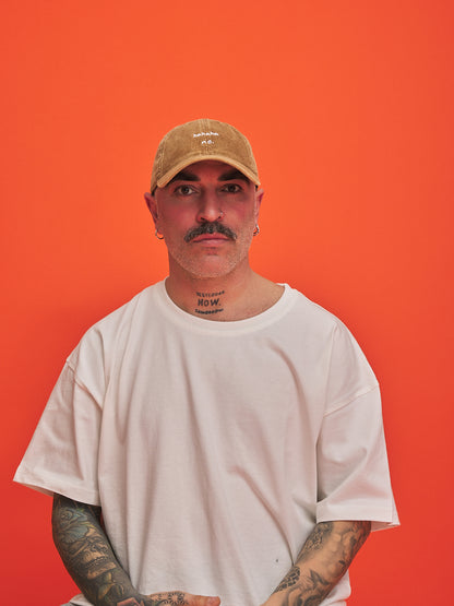 Man wearing Hahaha No Camel Corduroy Cap and white t-shirt against an orange background