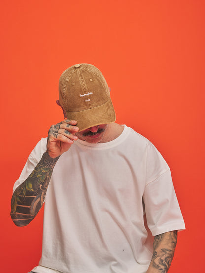 Person wearing Hahaha No Camel Corduroy Cap and white t-shirt against an orange background